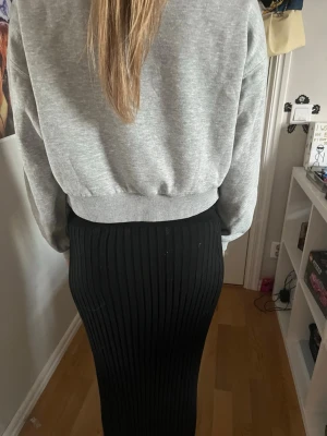 Svart ribbad långkjol - Säljer en svart ribbad långkjol med smal passform. Kjolen har en enkel och stilren design med vertikala ribbor som ger en snygg struktur. Perfekt att matcha med en croppad tröja eller hoodie. Passar även S och M.