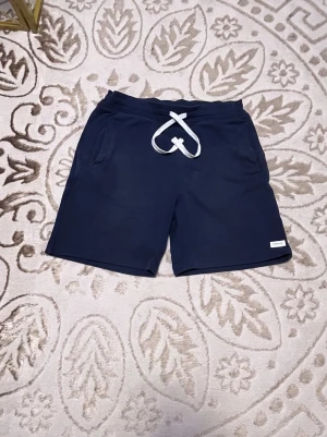 Mörkblå shorts med snörning - Mörkblå shorts med vit snörning i midjan och fickor på sidorna samt en bakficka. Perfekta för sommaren och tillverkade i mjuk bomull för en skön känsla.