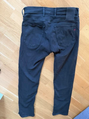 Svarta slim fit jeans från Replay - Säljer ett par svarta slim fit jeans från Replay, modell Grover. Jeansen har klassisk femficksdesign, bälteshällor och diskret Replay-logga på bakfickan. Snygg och enkel stil som passar till det mesta.