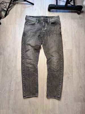 Grå G-star Raw jeans - Säljer ett par grå G-star Raw jeans med klassisk femficksmodell och dragkedjegylf. Jeansen har en snygg, något sliten look och raka ben. Perfekta för dig som gillar en avslappnad men ändå stilren vibe.