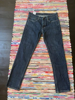 Mörkblå raka jeans från Levi's - Säljer ett par klassiska mörkblå jeans från Levi's med raka ben och femficksmodell. Jeansen har snygga kontrastsömmar och Levi's ikoniska läderpatch bak i midjan. Perfekta till alla dina outfits!