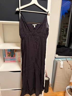 Svart långklänning  - Svart långklänning från H&M med smala axelband och v-ringad hals. Klänningen spänns åt med knytning i sidan av midjan på båda sidorna. Aldrig använt 