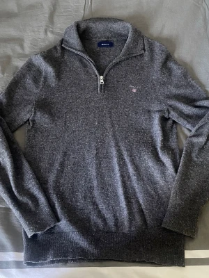 Grå stickad half zip tröja från Gant - Grö stickad tröja från Gant med half zip och liten broderad logga på bröstet. Tröjan har lång ärm  och hög krage. Perfekt för dig som gillar klassisk och stilren design. ⁉️skriv vid frågor ⁉️