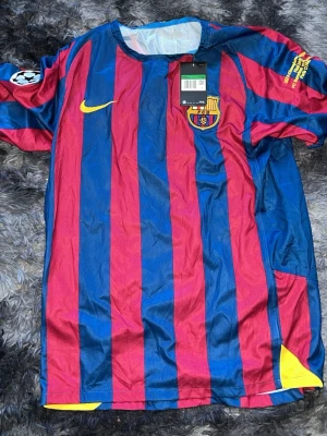 Barcelona Ronaldinho matchtröja - Säljer en klassisk Barcelona matchtröja från Nike med Ronaldinho och nummer 10 på ryggen. Tröjan har blå och röda vertikala ränder, klubbmärke på bröstet och Champions League-märke på ärmen. Tillverkad i lätt och ventilerande material.