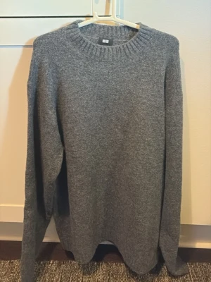 Grå stickad tröja från Uniqlo - Mysig grå stickad tröja från Uniqlo med rund halsringning och ribbade muddar. Perfekt för kyliga dagar och enkel att matcha med olika outfits. Tillverkad i mjukt material som känns skönt mot huden.