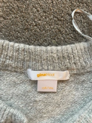 Ljusgrå kofta från Gina Tricot - Mysig ljusgrå kofta från Gina Tricot med rund halsringning och pärlknappar framtill. Koftan har långa ärmar och ribbade muddar vid ärmslut och nederkant. Perfekt att slänga på sig över en t-shirt eller linne.