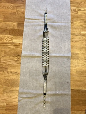 Svart och silverflätat bälte 96cm - Unikt bälte med flätad design i svart och silver. Bältet har metallringar som spänne och detaljer i både metall och syntetmaterial. Perfekt accessoar för att lyfta din outfit med en cool touch.