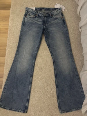 Blå bootcut jeans från Weekday - Bootcut jeans från Weekday i ljusblå tvätt med snygg slitning. Modellen heter NOVA och har låg midja. Tillverkade i en blandning av ekologisk och återvunnen bomull. Perfekta för dig som gillar en avslappnad men trendig look.
