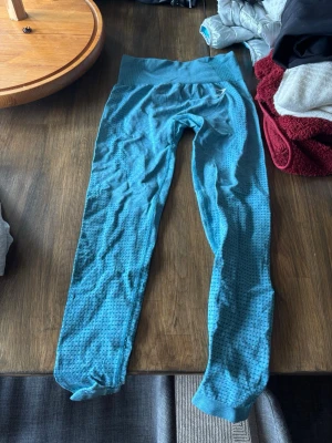 Blå seamless leggings från Gymshark - Blå seamless leggings från Gymshark med hög midja och diskret mönster längs benen. Tillverkade i ett stretchigt och andningsbart material som sitter skönt och följer kroppen. Bred ribbad linning för extra stöd och komfort.