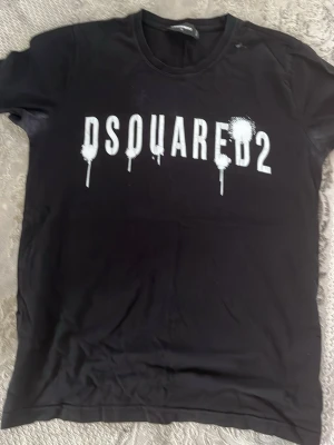 Svart Dsquared2 t-shirt med tryck - Snygg svart t-shirt från Dsquared2 med vitt tryck framtill. T-shirten har rund hals och korta ärmar. Materialet känns mjukt och skönt, troligtvis bomull. Perfekt för dig som gillar streetwear och vill sticka ut med ett coolt print.