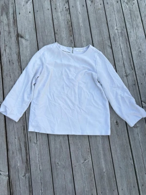 Vit blus med dragkedja bak - Stilren vit blus med rund halsringning och lång ärm. Blusen har en rak passform och en snygg silverfärgad dragkedja i ryggen som detalj. 