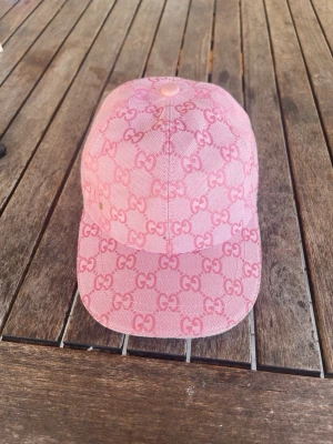 Rosa keps med GG-mönster - Snygg rosa keps med klassiskt GG-mönster över hela kepsen. Kepsen har böjd skärm och en knapp på toppen. Perfekt accessoar för dig som vill sticka ut med en trendig och ungdomlig look.
