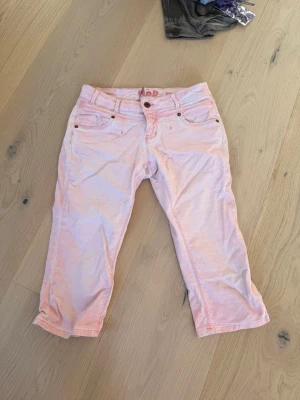 Ljusrosa lågmidjade capri jeans från MOD - Säljer ett par ljusrosa low waist capri jeans från MOD i storlek 28. Jeansen har fem fickor, raka ben och klassisk knappgylf. Snygga kontrastsömmar och detaljer i kopparfärg. Perfekta för dig som vill ha en unik och färgglad look. Helt ny med prislapp