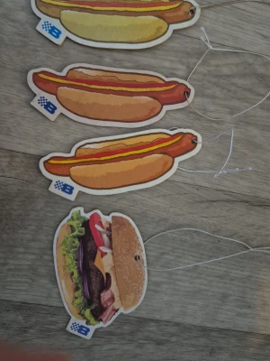 Hängande doftkort i matmotiv - Fyra hängande doftkort i form av hamburgare och korv med bröd. Färgglada illustrationer med detaljer som sallad, ost, ketchup och senap. Tillverkade i papper med snöre för upphängning. Perfekt som rolig accessoar till väskan eller rummet.