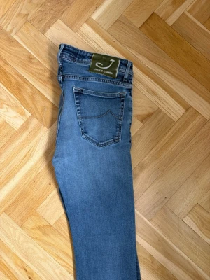 Blå raka jeans från Jacob Cohen - Snygga blå jeans från Jacob Cohen med raka ben och klassisk femficksmodell. Jeansen har en ljus tvätt med subtila slitningar och patch med logga bak i midjan. Tillverkade i mjukt denimtyg som ger en skön känsla och stilren look.