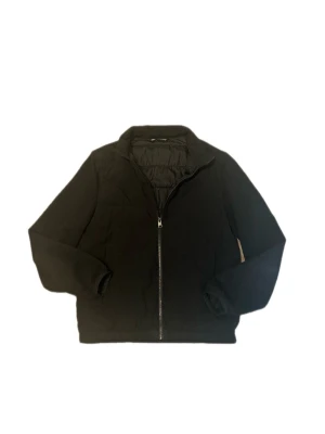 Cadigan från Zara - Stilren svart cardigan från Zara med hel dragkedja framtill och hög krage. Jackan har lång ärm och enkel design som passar till många olika outfits. Perfekt för kyligare dagar och ger en clean look.