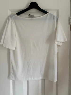 Vit t-shirt från H&M, XS - En enkel och stilren vit t-shirt från H&M i storlek XS. T-shirten har rund halsringning och korta ärmar. Tillverkad i mjuk bomull som känns skön mot huden. Perfekt basplagg till garderoben. Passar mig som är mer än S.