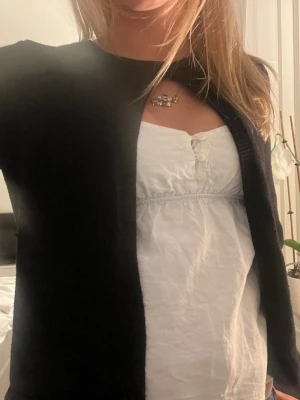Svart kofta med rund hals - En klassisk svart kofta med rund hals och lång ärm. Koftan har en enkel knäppning framtill och är i ett mjukt material. Stilren och lätt att matcha med olika outfits.