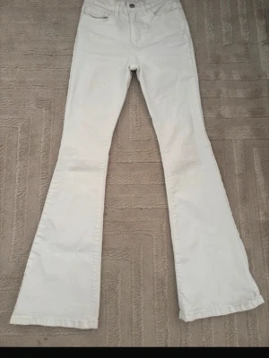 Vita utsvängda jeans - Säljer ett par vita jeans med utsvängda ben. Klassisk femficksmodell med knapp och dragkedja framtill. 