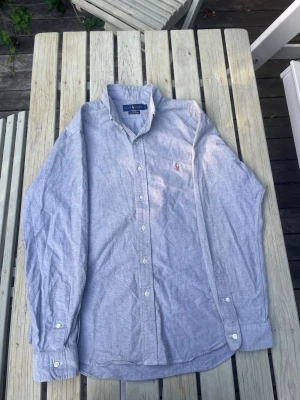Ralph Lauren Ljusblå Oxford-skjorta Slim Fit | Stl L - Klassisk ljusblå långärmad Oxford-skjorta från Polo Ralph Lauren i Slim Fit, storlek L. Bra begagnat skick, ett måste i basgarderoben. 