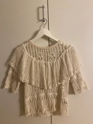 Beige virkad blus med volang - Superfin beige virkad blus med volangdetalj över axlarna och trekvartsärm. Blusen har ett luftigt, mönstrat stickat material. Köpte tröjan från Zara, i storlek S. Endast andvänd några få gånger.