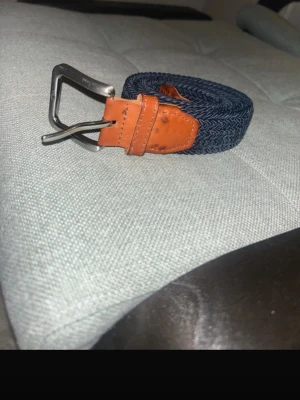 Blå flätat bälte  - Snyggt marinblått flätat bälte från Jack & Jones med detaljer i brunt skinn och silverfärgat spänne. Perfekt accessoar för att lyfta din outfit med en stilren touch. Bältet har en klassisk design och passar till många olika looks.