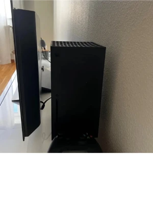 Xbox Series X spelkonsol - Säljer en Xbox Series X spelkonsol i mattsvart färg med stilren, rektangulär design och ventiler i toppen med gröna detaljer. Konsolen är tillverkad i plast och metall och levereras med en svart trådlös handkontroll samt originalkartong.