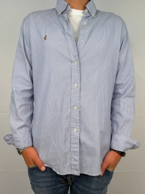 Ralph lauren skjorta vit/blå randig M - Säljer denna magiskt fräscha ralph lauren skjorta. Riktigt skönt material . Size 15 1/2 som motsvarar M. Modellen är 180cm. Bredd 50cm,  längd 72cm! Fint skick, nytvättad och ny strykt så att skillnaden på denna och en ny ska vara minimal! Tyvärr har en knapp lossnat, går att sätta dit lätt om man vill! Fraktar samma dag som köp, kan gå ner i pris vid snabb affär! 🤩