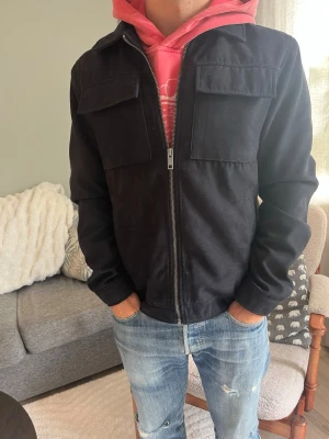 Svart overshirt med dragkedja - Jack & Jones jacka i svart mocka/suede med blixtlås fram, kort/klassisk passform och två stora lockfickor på bröstet. Fint material med len yta, funkar som overshirt eller lätt jacka.  Skick: bra skick, inga hål eller fläckar Material: mocka/suede Storlek: M Modell: 175 cm / 65 kg — sitter true to size på bild  