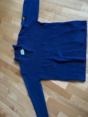 Mörkblå stickad tröja med halvzip - Mörkblå stickad tröja från Calvin Klein jeans med halv dragkedja framtill och ribbade muddar. Tröjan har lång ärm och en liten patch på ena ärmen. Perfekt för lager på lager och enkel att styla till olika outfits. Vid minsta funderingar hör bara av er 😁