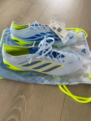 Adidas Predator FG (firm ground) elite fotbollsskor - Säljer ett par Adidas Predator fotbollsskor i ljusblått med neon-gula och mörkblå detaljer. Skorna har snörning, låg profil och är tillverkade i syntetmaterial. Nya med lappar. Nypris 3199kr, påse ingår.