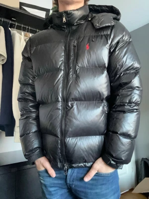  Polo Ralph Lauren dunjacka/pufferjacka – svart, glansig, huva - Säljer min pufferjacka från Polo Ralph Lauren i mörkblått glansigt material med den klassiska röda pony-loggan på bröstet. Jackan har avtagbar/justerbar huva, dragkedjefickor både på bröstet och sidorna, samt stickade manschetter som håller kylan ute. Ett riktigt snyggt och varmt plagg som funkar lika bra till vardags som till en snyggare vinterlook. Jackan är i fint skick utan hål, fläckar eller trasiga dragkedjor – bara normalt brukslitage. Rökfritt hem.