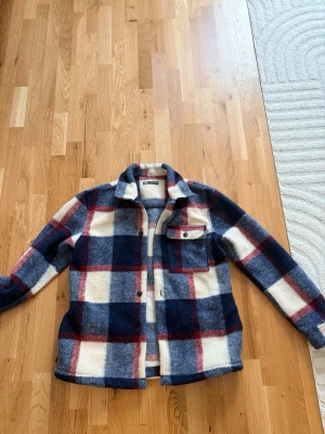 Jacka -Zara  - Säljer en snygg overshirt/jacka från Zara med rutigt mönster i blått, vitt och rött. Jackan har en bröstficka med knapp, klassisk krage och knäppning framtill. Materialet är mjukt och lite fluffigt, perfekt för lager på lager.