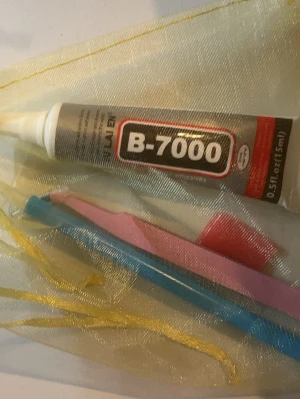 B-7000 lim och verktygskit - Säljer ett kit med B-7000 lim (15 ml) och flera små verktyg i olika färger, perfekt för pyssel, hobby eller reparationer. Allt ligger i en genomskinlig påse med gula band. Limmet är i tub och verktygen är i plast.