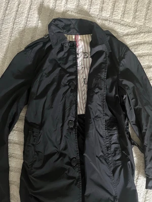 Kappa J.Lindeberg - Snygg svart Kappa från J.Lindeberg med klassisk design. Perfekt för blåsiga dagar och enkel att matcha till olika outfits.