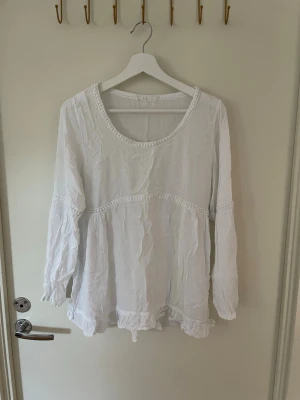 Vit bohemisk sommar blus, stl M bomull oanvänt  - Luftig vit blus med rund halsringning och dekorativa spetsdetaljer. Blusen har långa ärmar och volangkant nedtill, vilket ger en bohemisk och avslappnad look. Perfekt att matcha med jeans eller kjol för en trendig stil. Stl M 