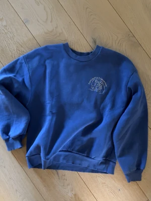 Blå sweatshirt från Gina Tricot - Blå sweatshirt från Gina Tricot med rund halsringning och ribbade muddar. Tryck på bröstet med texten 'Every body is a beach body' och en stiliserad illustration. Perfekt för en avslappnad och cool stil.