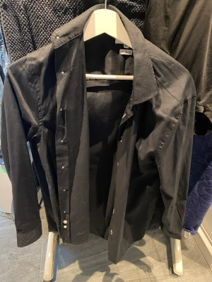 Svart skjorta från Approach XS - Klassisk svart skjorta från Approach i storlek XS. Skjortan har lång ärm, knappar framtill och en enkel, stilren design. Casual fit som ger en avslappnad men snygg look. Perfekt till jeans eller chinos.