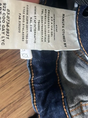Mörkblåa Dsquared jeans - Säljer ett par mörkblå jeans med slitningar, färgstänk i vitt och gult samt snygga detaljerade sömmar. Jeansen har klassisk femficksmodell och orange kontrastsömmar. Materialet är denim i bomull. Perfekta för dig som gillar en trendig och avslappnad stil.