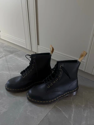 Dr Martens - Säljer ett par svarta kängor i läder med klassiska gula sömmar runt sulan och högt skaft. Kängorna har snörning framtill och en gul flärp på baksidan. Endast använda en gång🥰