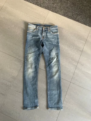 Nudie jeans - Säljer ett par klassiska blå jeans med raka ben med snygg tvätt. Jeansen har fem fickor, normal midja och kontrastsömmar. Perfekta till en avslappnad stil. 