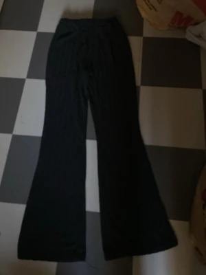 Svarta bootcut byxor med diskreta ränder - Säljer ett par svarta byxor med diskreta vertikala ränder och bootcut-modell. Byxorna har hög midja och är perfekta för dig som gillar en klassisk men trendig look. Materialet känns mjukt och bekvämt.