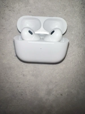 Apple AirPods Pro (1st or 2nd Generation) - The images show a pair of Apple AirPods Pro in their charging case. The first image displays the earbuds inside the open case, while the second image shows the closed case from the back, highlighting the pairing button and hinge. These wireless earbuds are known for their active noise cancellation, transparency mode, and customizable fit with silicone ear tips.
