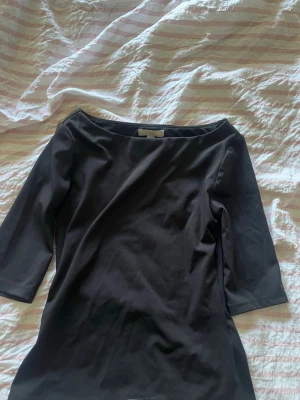 Svart topp med trekvartsärm - En stilren svart topp med bred urringning och trekvartsärm. Toppen har en enkel, elegant design och är gjord i ett mjukt, stretchigt material som sitter snyggt på kroppen. Perfekt att matcha med jeans eller kjol för en clean look.