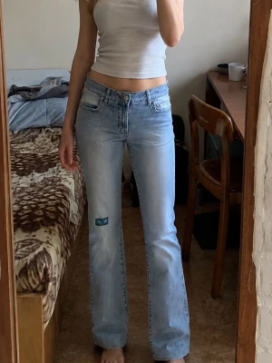 Vigoss Jeans W30 L32 – ljusblå bootcut jeans - Ljusblå jeans från Vigoss Jeans i storlek W30 L32. Snygg Y2K-inspirerad modell med låg/normal midja och lätt utsvängda ben. Klassisk ljus tvätt med slitna/faded detaljer och dekorativa bakfickor. Liten dekorativ patch på ena benet.  Material: 76% bomull, 22% Tactel nylon, 2% elastan.  Fint begagnat skick. Se bilder för passform och detaljer.