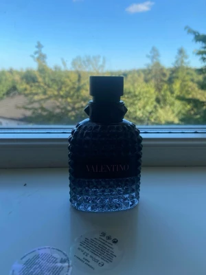 Valentino parfym med nitar och mönster - Säljer en snygg parfym från Valentino i en genomskinlig glasflaska med coolt nitmönster och svart lock. Flaskan har en lyxig känsla och är perfekt för dig som gillar exklusiva dofter och stilren design. 50 ml ca 10-15 kvar 