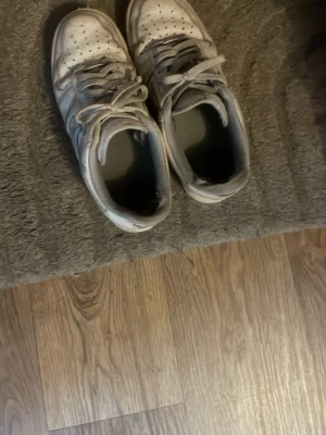 Vita låga sneakers med snörning - Säljer ett par vita sneakers med klassisk låg profil och snörning. Skorna har perforerade detaljer på tån och en tydlig sula. Materialet är syntet och textil, och designen är enkel men stilren. Perfekta för dig som gillar streetwear och sportig look.