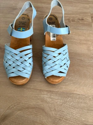 Ljusblå flätade sandaler med träbotten - Säljer ett par ljusblå sandaler med flätad design och justerbart ankelband. Sandalerna har en klassisk träbotten och öppen tå, vilket ger en retro och somrig vibe. Perfekta för dig som gillar stilrena och bekväma skor i naturmaterial. Kolla gärna mina andra annonser❗️