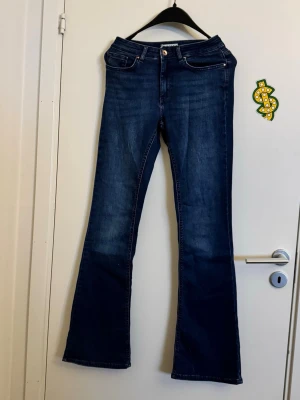 Mörkblå bootcut jeans från ONLY - Snygga mörkblå bootcut jeans från ONLY med klassisk femficksdesign och orange sömmar. Jeansen har en lätt utsvängd passform nertill och är tillverkade i denim med en skön stretch. Perfekta för dig som gillar en retroinspirerad look.