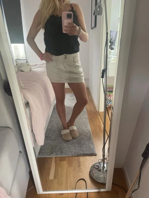 Beige kortkjol med knappar - Snygg beige kortkjol med dubbla knappar framtill och fickor på sidorna. Kjolen har en enkel och stilren design som passar perfekt till sommaren. Tillverkad i ett mjukt bomullsmaterial för en bekväm känsla.